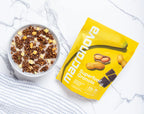 A bowl of Choc-Peanut Banana granola with milk beside its Macronova pouch.