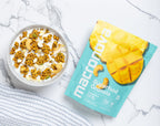 A bowl of Pineapple Mango granola with milk beside its Macronova pouch.