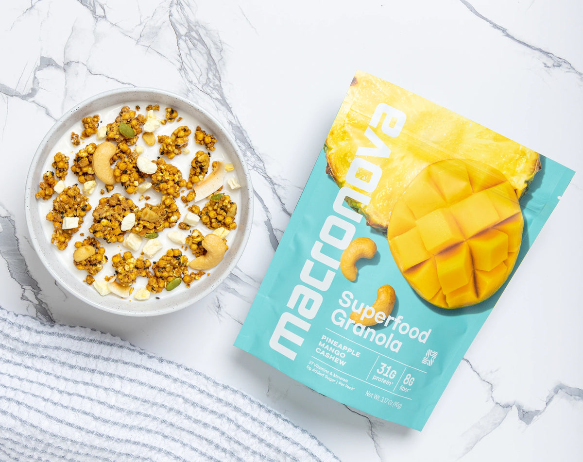 A bowl of Pineapple Mango granola with milk beside its Macronova pouch.